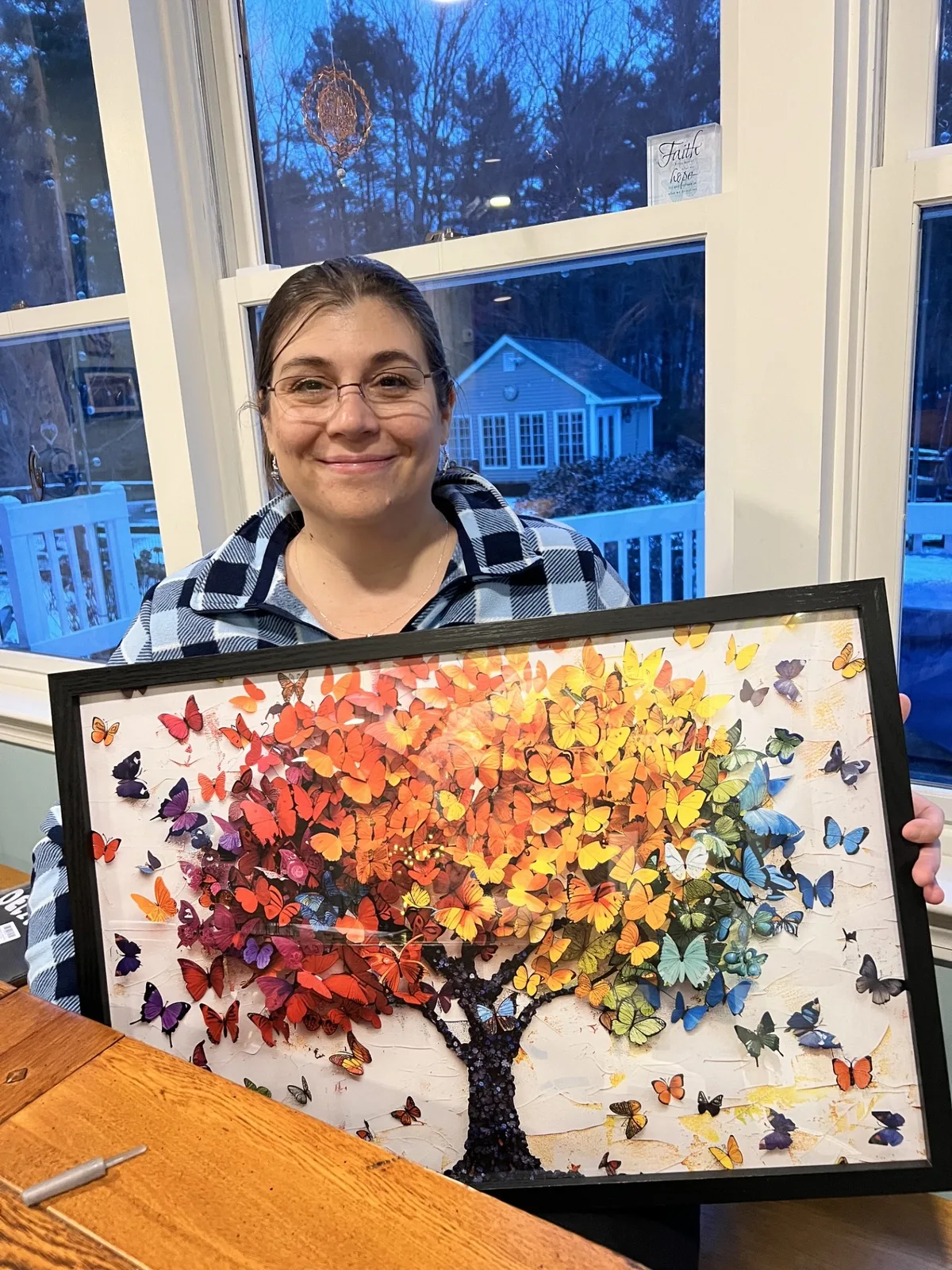 A woman holding a framed butterfly-and-tree artwork in a bright room